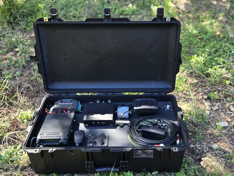 The Pelican case radio kit open on gravel and grass, with its radio gear mounted inside the case.